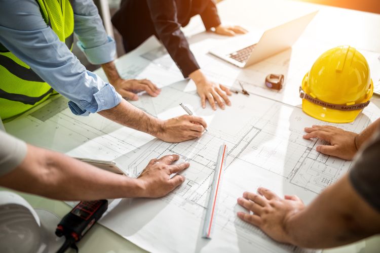 A hardhat rests on architectural plans while construction professionals review the details.